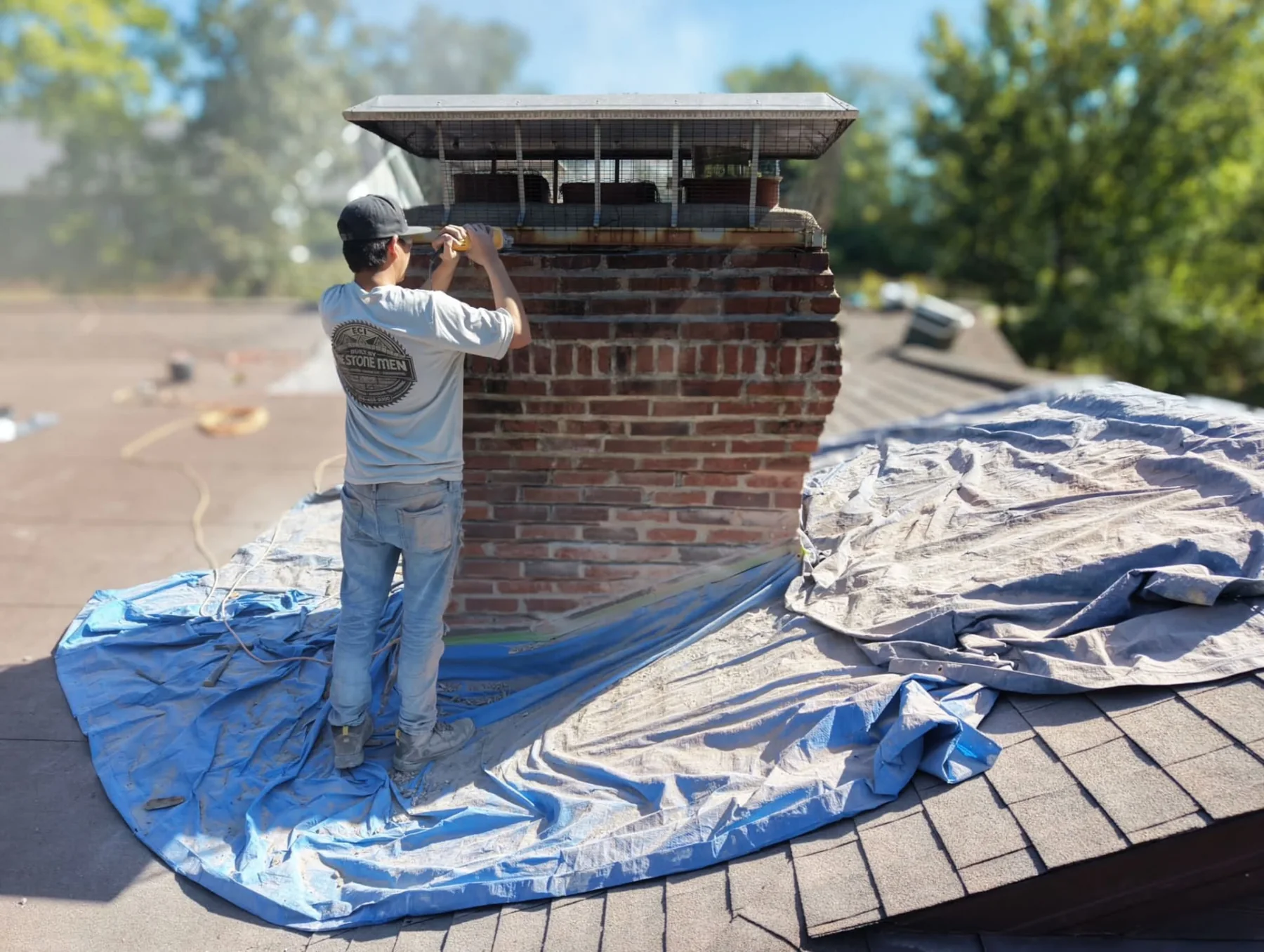 ECI mason repairing a brick chimney on a Missouri home, with protective tarps on the roof