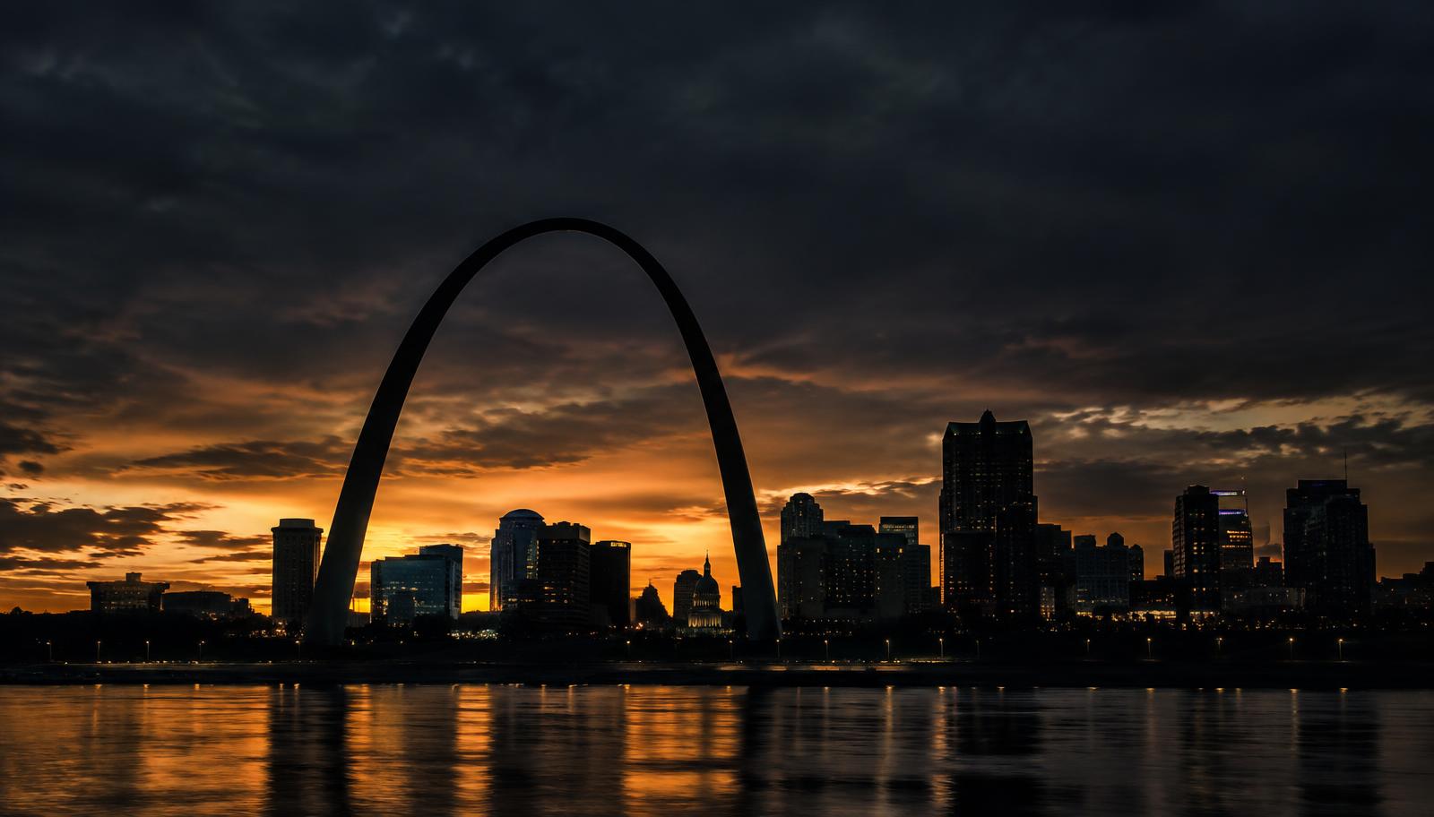 St. Louis skyline at dusk with the Gateway Arch silhouetted against a golden sky